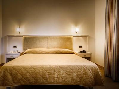 Hell beleuchtetes Hotelzimmer mit Doppelbett und beigen Vorhängen