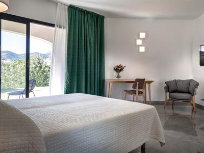 Helles Hotelzimmer mit großem Bett, grünem Vorhang, Balkon und modernem Mobiliar.