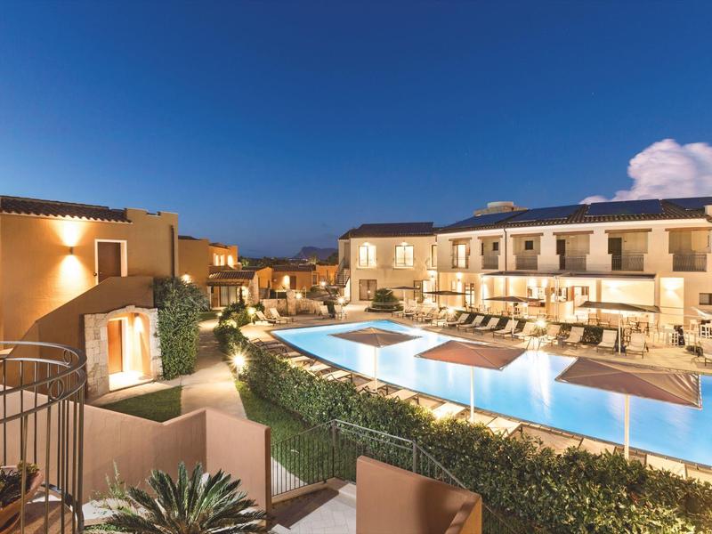 Abendaufnahme eines eleganten Hotels mit beleuchtetem Pool und Sitzbereichen im Freien unter klarem Himmel.