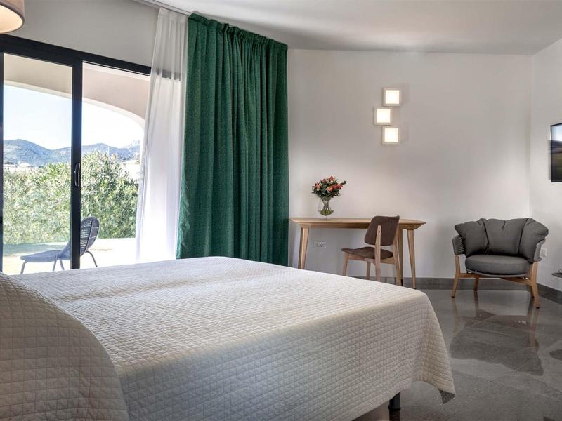 Helles Hotelzimmer mit großem Bett, grünem Vorhang, Balkon und modernem Mobiliar.