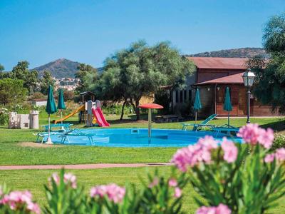 Zwembad met waterspel en glijbaan voor een vakantiehuis met bomen en bergen op de achtergrond.