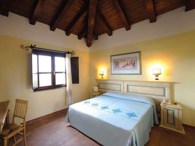 Lichte hotelkamer met tweepersoonsbed, houten meubels en zichtbare plafondbalken.