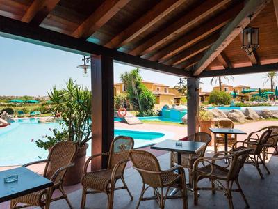 Terrasse couverte avec tables et chaises à côté d'une piscine dans une station de vacances.