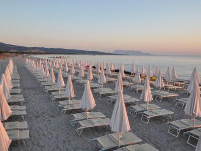Rangées de transats avec parasols fermés sur une plage calme au coucher du soleil.