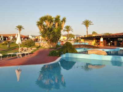 Zone de piscine avec parasols, palmiers et eau calme dans une station de vacances