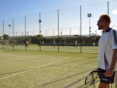 Un homme avec une raquette de tennis se tient sur un court de tennis en plein air au soleil.