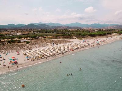Lange zandstrand met ligbedden en parasols, duinen en bergen op de achtergrond onder een bewolkte lucht.