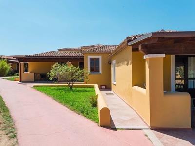 Maison de vacances jaune avec toit rouge et verdure sous ciel bleu