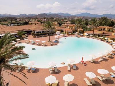 Grand bassin rond d'hôtel avec transats et parasols, entouré de paysage et de montagnes.