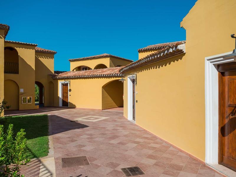 Gele gebouwen met rode daken langs een geplaveid pad onder een heldere blauwe lucht.