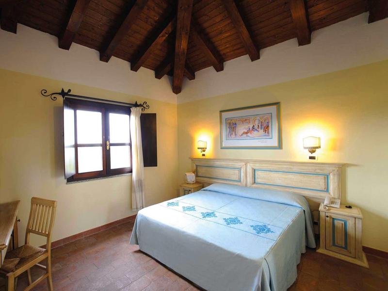 Lichte hotelkamer met tweepersoonsbed, houten meubels en zichtbare plafondbalken.