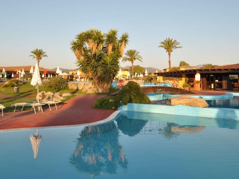 Groot zwembad bij zonsondergang met palmbomen en hotelgebouwen op de achtergrond.
