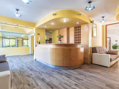 Reception dell'hotel con banco in legno rotondo, poltrone comode e design luminoso.