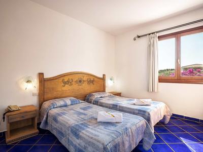 Simple twin room with two single beds, wooden furniture, and window overlooking outdoor area.