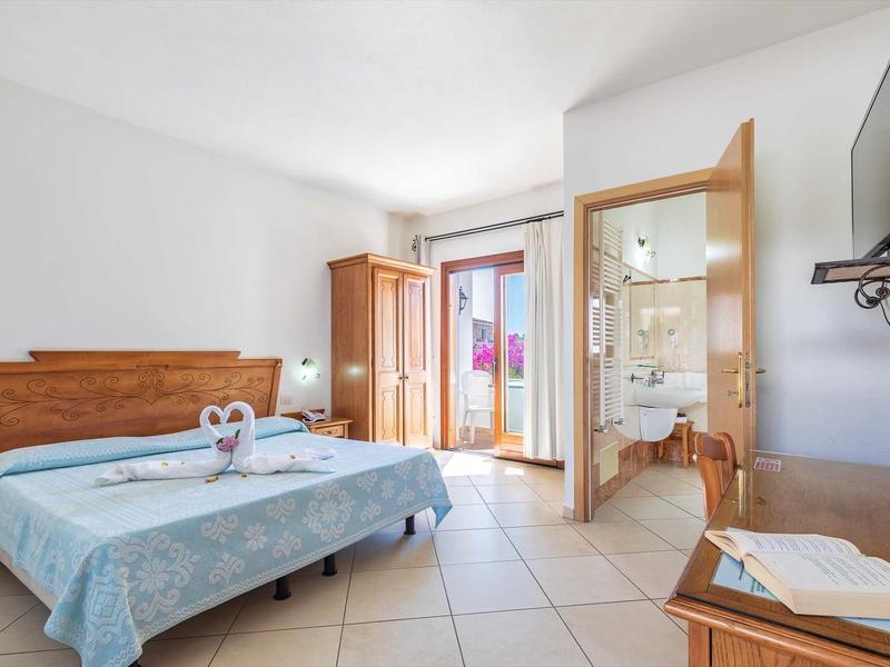 Bright hotel room with double bed, balcony, wooden furniture, and flat-screen TV.