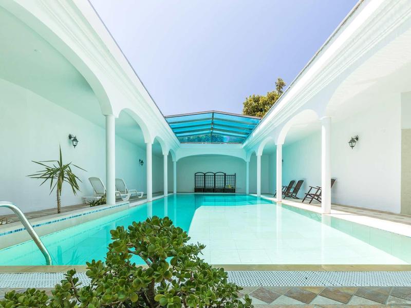 Modern pool area with blue glass roof, white facade, and lounge chairs.