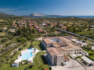 Aerial view of a hotel with swimming pool, surrounded by greenery and mountains in the background.