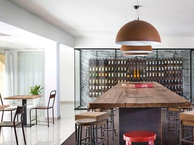 Modern dining area with long wooden table, high stools, and wine rack in bright room.
