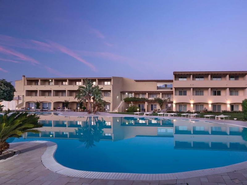 Large multi-story hotel building with a spacious pool in front at sunset.