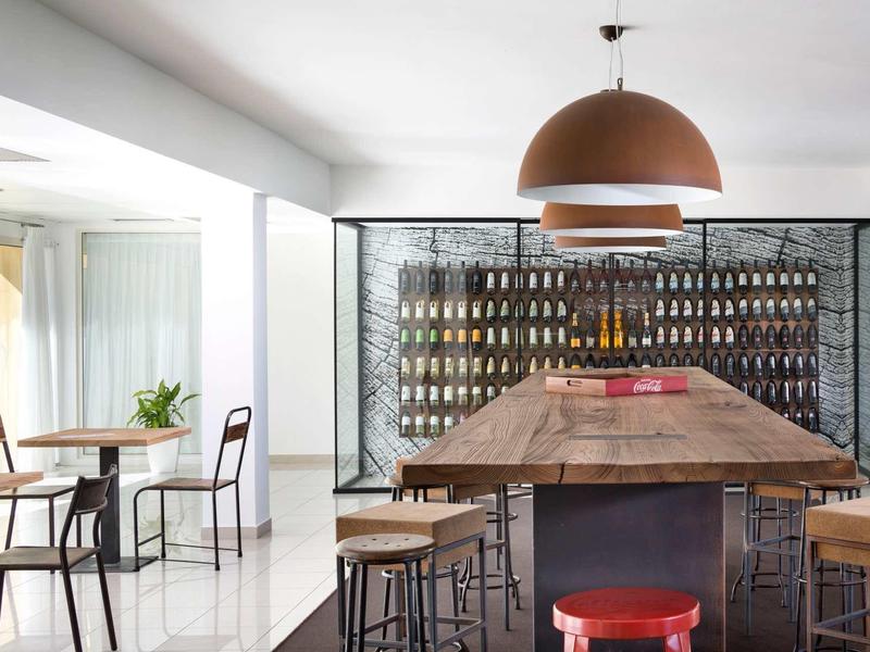 Modern hotel wine cellar with large wooden table and many wine bottles on shelves.