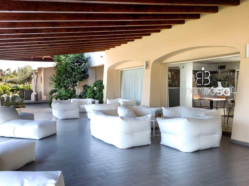 Covered terrace with white armchairs in front of a hotel restaurant.