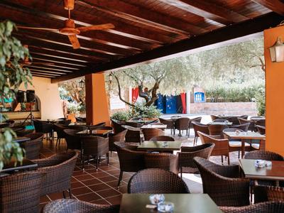 Überdachte Terrasse mit Holzdach, Korbstühlen und Tischen, umgeben von Pflanzen und Blick ins Freie.