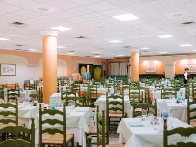 Großer, hell beleuchteter Speisesaal mit vielen Holztischen und Stühlen, weiß gedeckt.