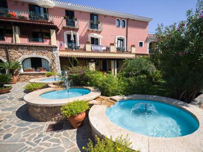 Giardino dell'hotel con due vasche idromassaggio rotonde e vegetazione rigogliosa davanti a un edificio rosa.