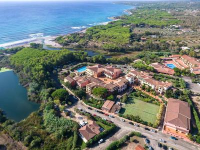 Luftaufnahme einer Küstenregion mit Gebäuden, Grünflächen, einem See und blauem Meer im Hintergrund.