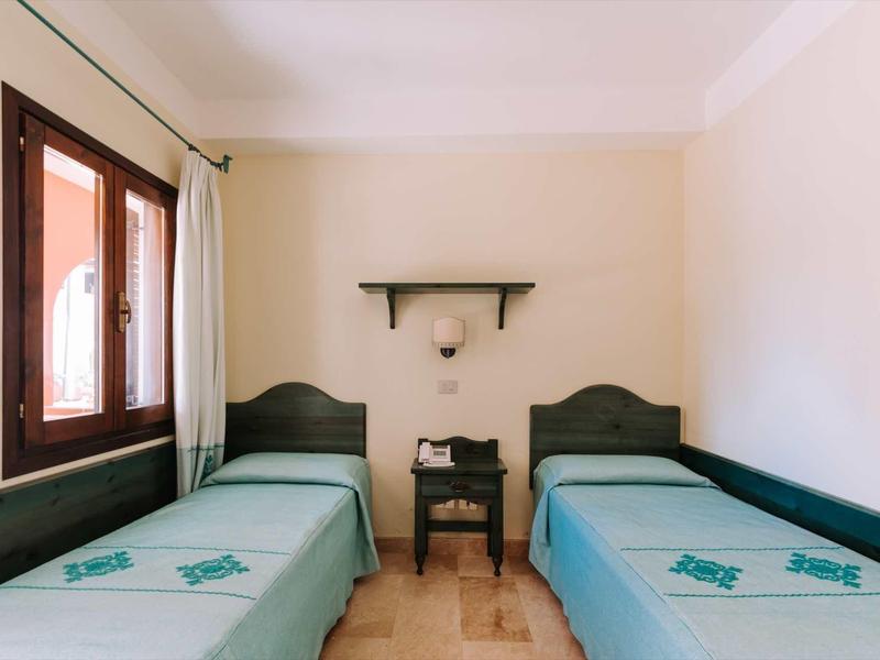 Zimmer mit zwei Einzelbetten, blauen Bettlaken, kleinem Nachttisch und hellem Wandanstrich.