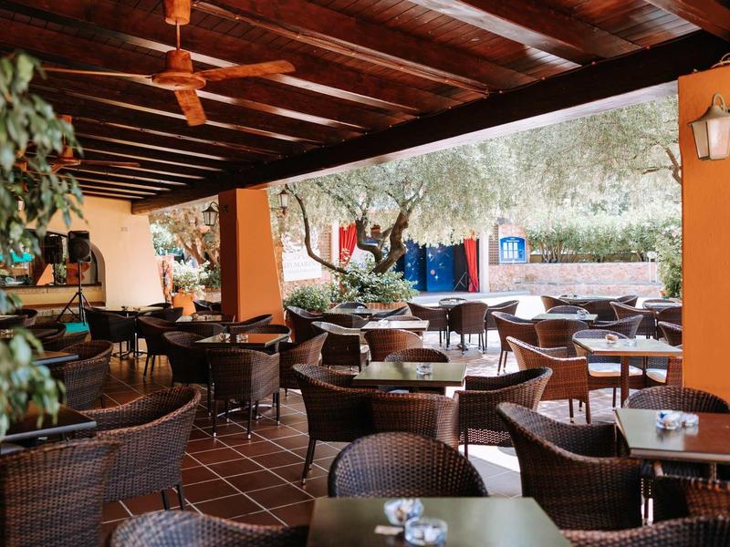 Überdachte Terrasse mit Holzdach, Korbstühlen und Tischen, umgeben von Pflanzen und Blick ins Freie.