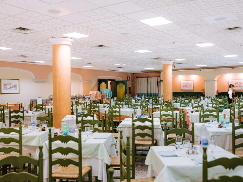 Großer, hell beleuchteter Speisesaal mit vielen Holztischen und Stühlen, weiß gedeckt.