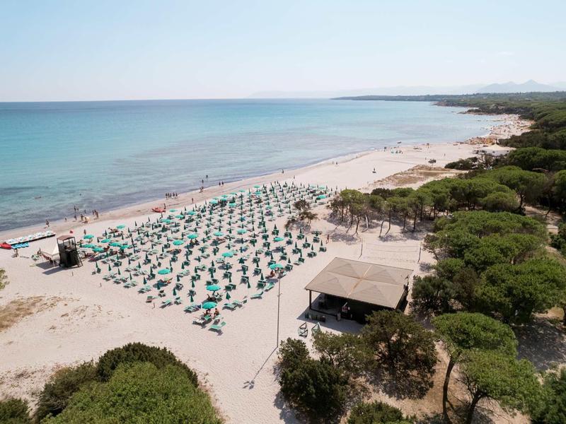 Strand mit vielen grünen Sonnenschirmen, weißem Sand und blauem Meer, umgeben von grüner Vegetation.