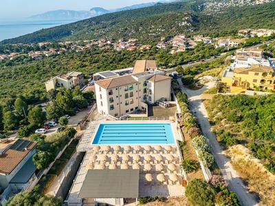 Vista aerea di un hotel con una grande piscina e colline circostanti con il mare sullo sfondo.