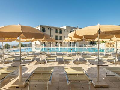 Terrazza dell'hotel con più lettini e ombrelloni vicino alla piscina sotto un cielo sereno