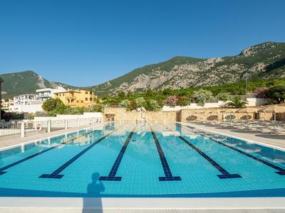 Grande piscina all'aperto con montagne sullo sfondo e lettini ai bordi