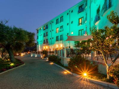 Edificio dell'hotel illuminato con giardino e percorso lastricato al crepuscolo.
