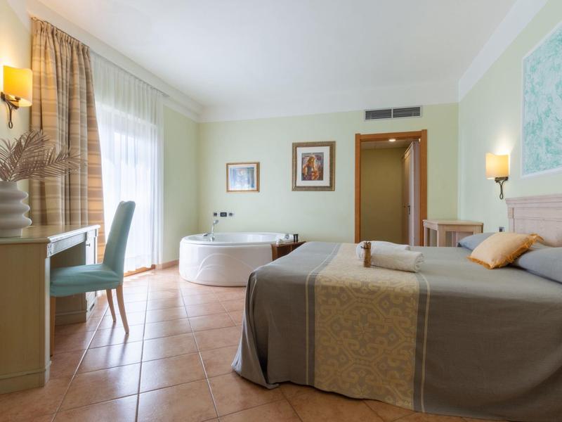 Camera d'hotel luminosa con letto matrimoniale, scrivania, sedia e vasca da bagno accanto alla finestra.