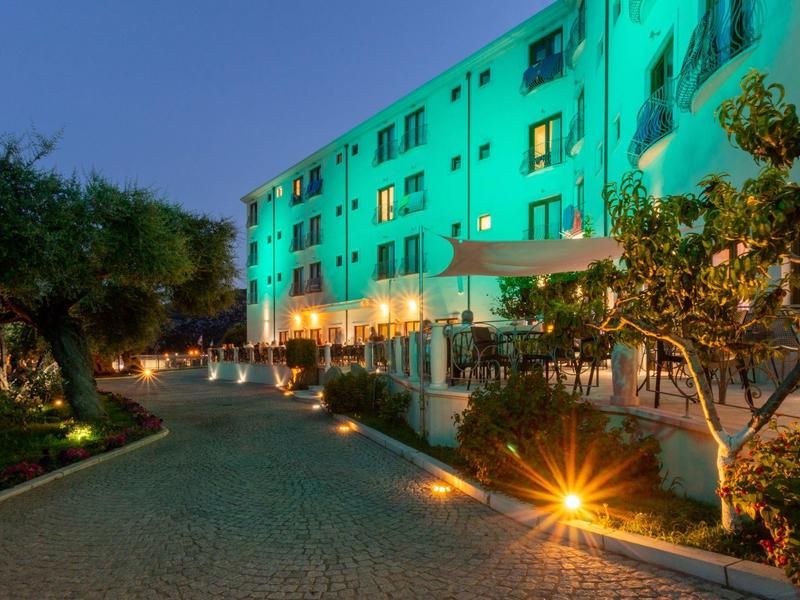 Edificio dell'hotel illuminato con giardino e percorso lastricato al crepuscolo.