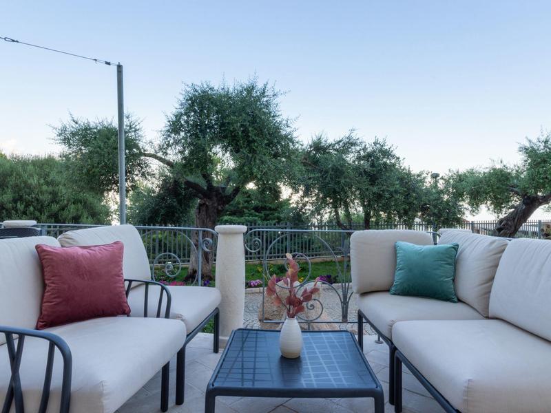 Area lounge moderna sulla terrazza con cuscini e vista sugli alberi sotto un cielo limpido.