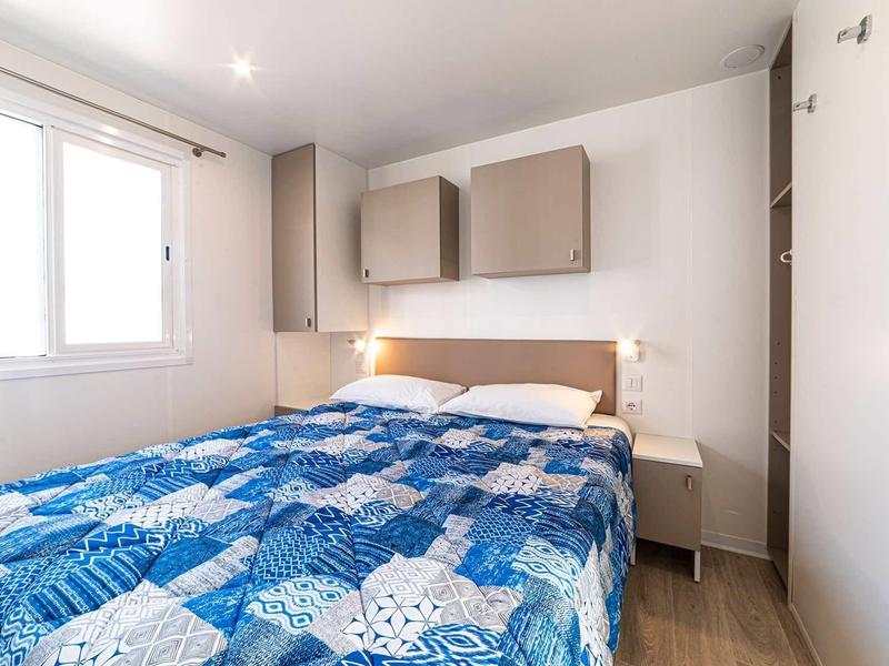 Petite chambre avec lit double, couverture bleue et rangements dans un camping-car.