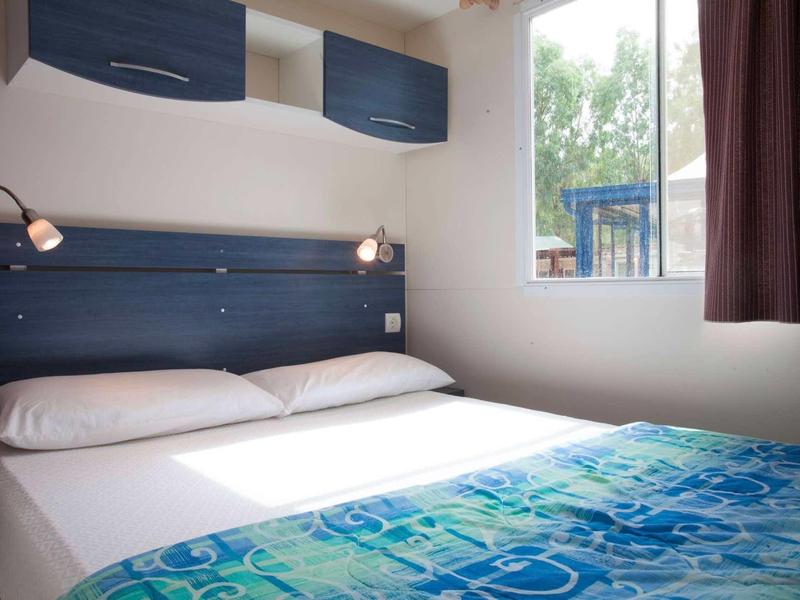 Chambre double simple avec couvre-lit bleu et fenêtre donnant sur le jardin