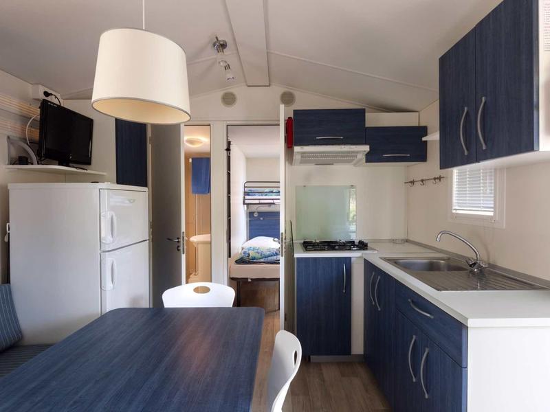 Petite kitchenette avec armoires bleues, réfrigérateur blanc et table à manger avec chaises.