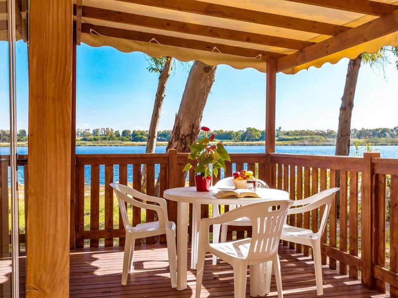 Terrasse confortable avec table et chaises, vue sur le lac et les arbres par temps ensoleillé.
