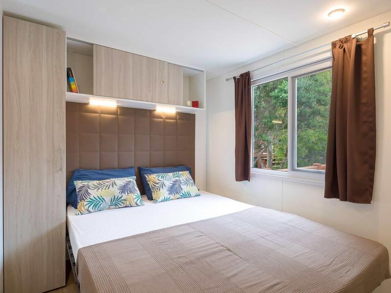 Chambre moderne avec lit double, rideaux marron et armoires en bois près de la fenêtre.