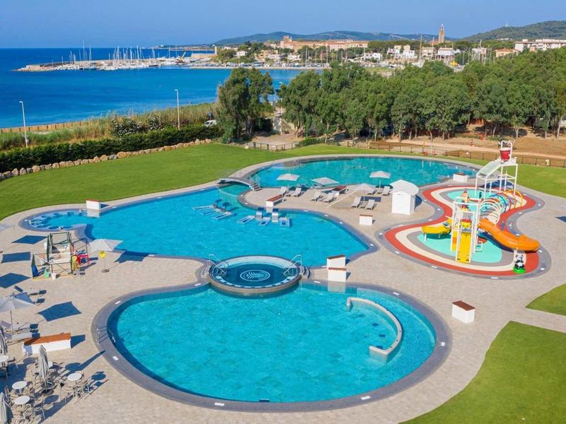 Grande piscine extérieure avec toboggans, transats et vue sur la mer et la ville côtière.