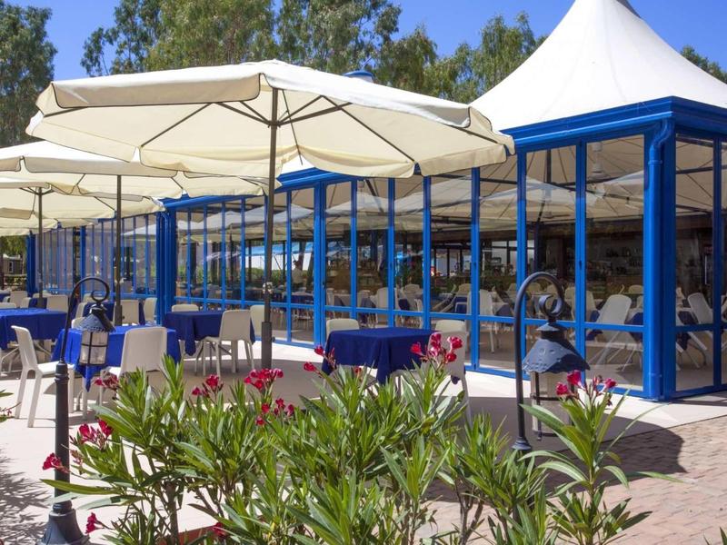 Restaurant en plein air avec parasols blancs, tables bleues et plantes vertes par une journée ensoleillée