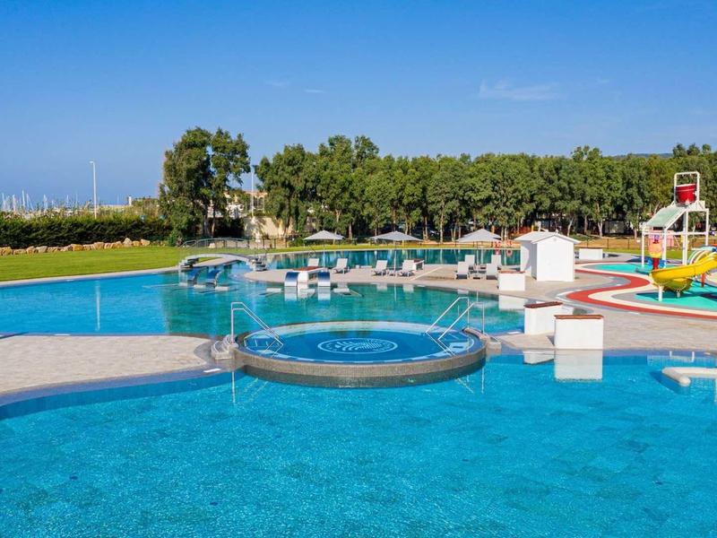 Grande piscine extérieure avec bain à remous séparé et toboggans aquatiques dans un paysage ensoleillé.