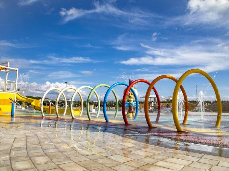 Aire de jeux aquatique colorée avec des anneaux arc-en-ciel et des jets d'eau sous un ciel bleu.