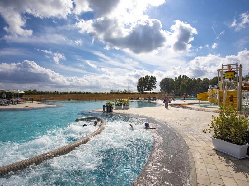 Piscine à vagues avec éclaboussures d'eau et toboggans jaunes sous un ciel nuageux dans une station de vacances.